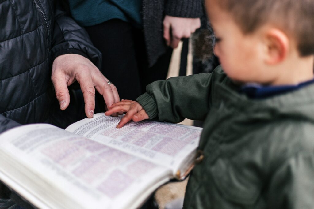 A young boy and a parent put their hands on the pages of a Bible