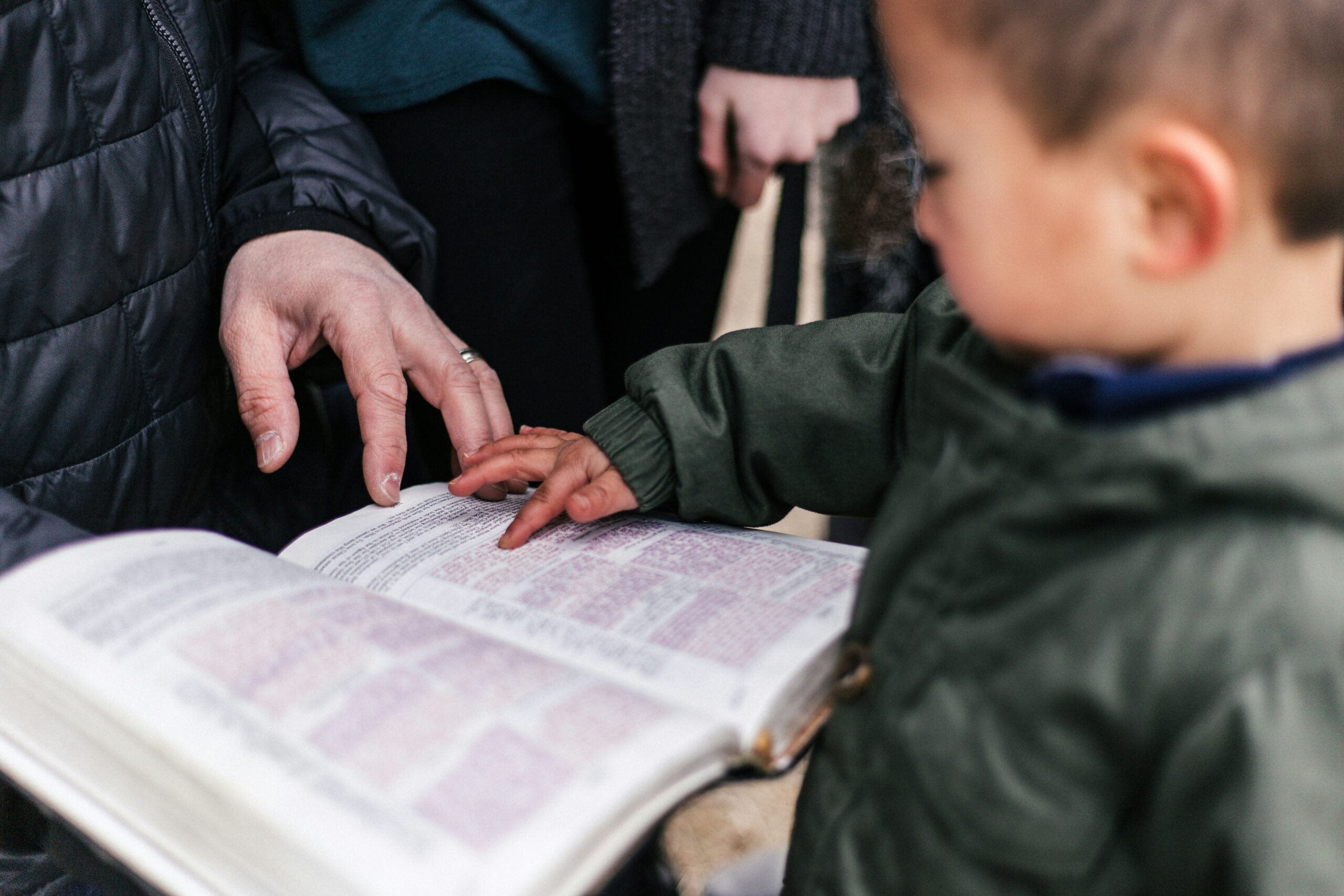 A young boy and a parent put their hands on the pages of a Bible