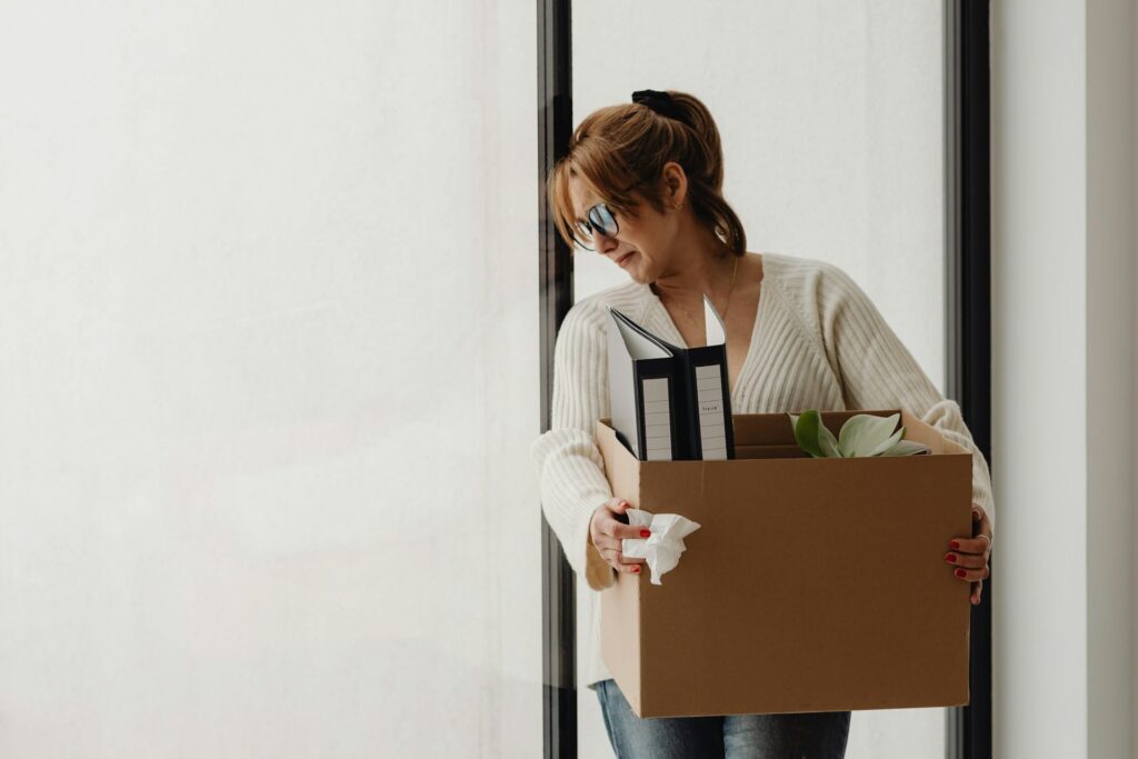 Woman with a sad expression leaving a workplace with a cardboard box full of items
